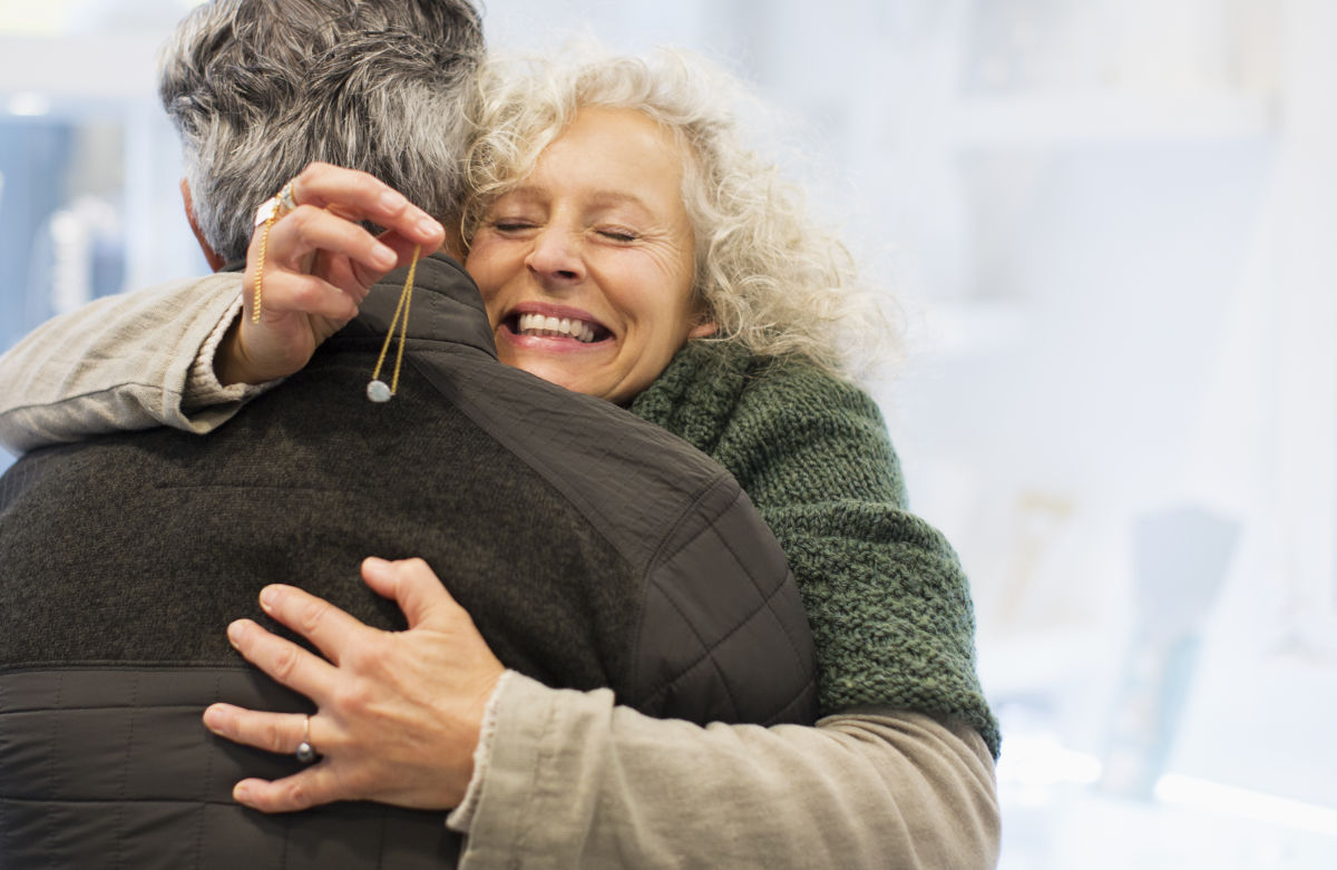 Smiling lady hugging a man with a necklace in her hand.