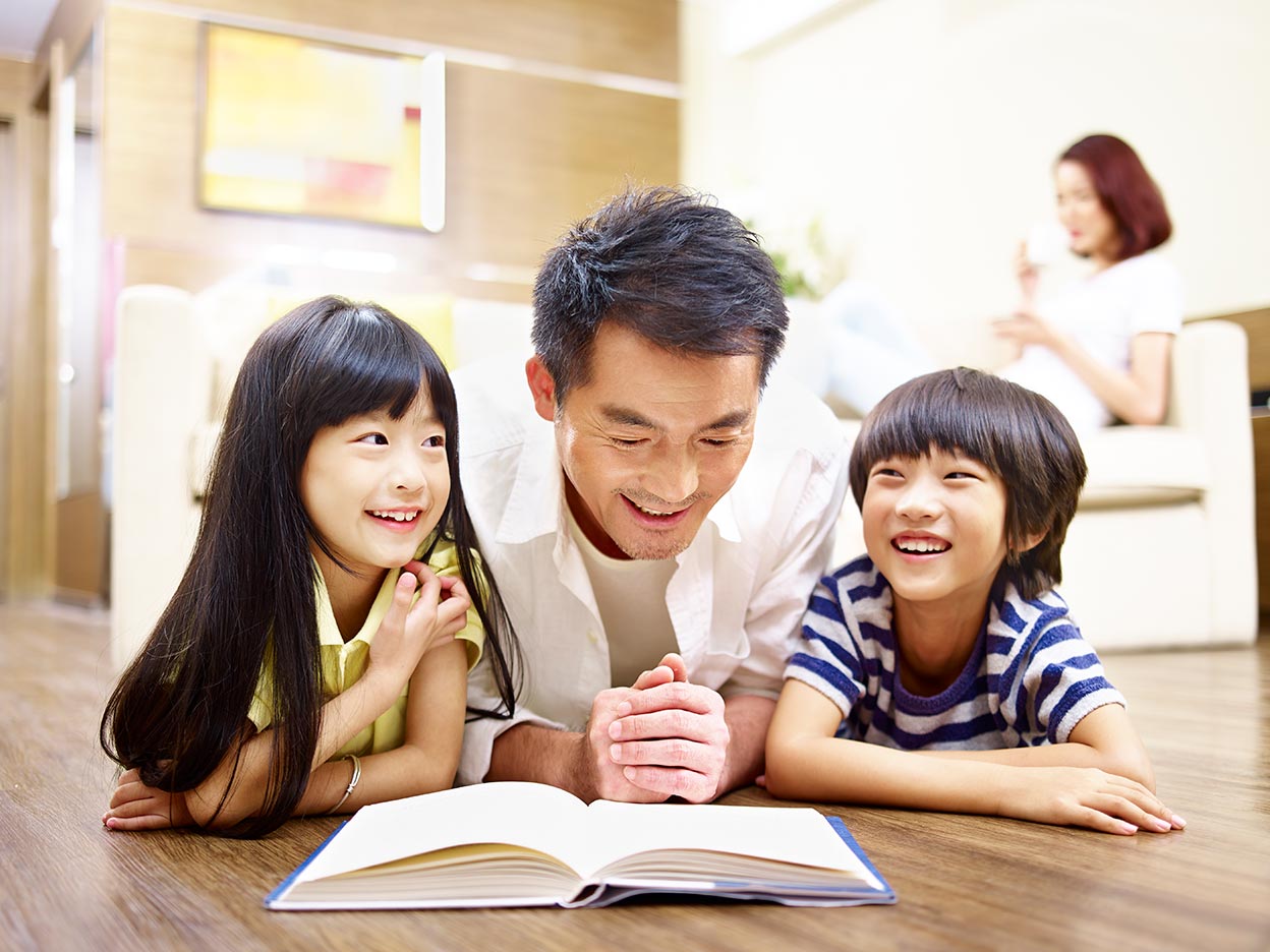 Father and two children laying on the floor reading a book.