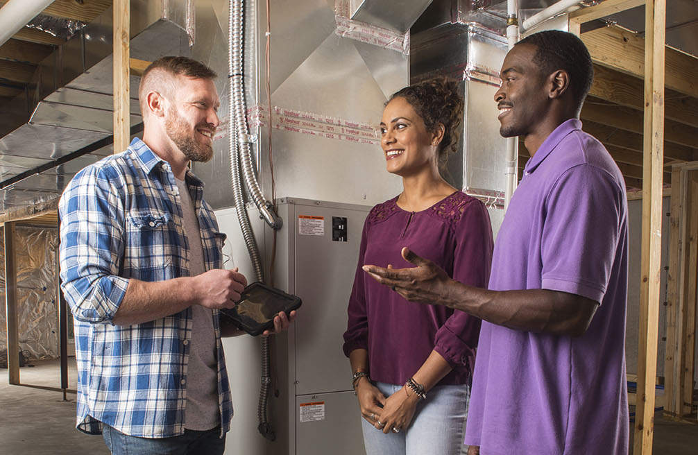Couple and HVAC professional standing in unfinished basement discussing financing.